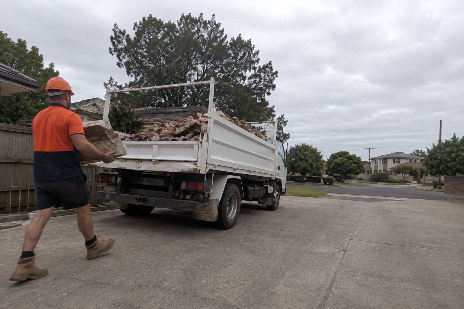 A Demo Bros crew member clearing heavy brick rubble beside the truck on a Melbourne job